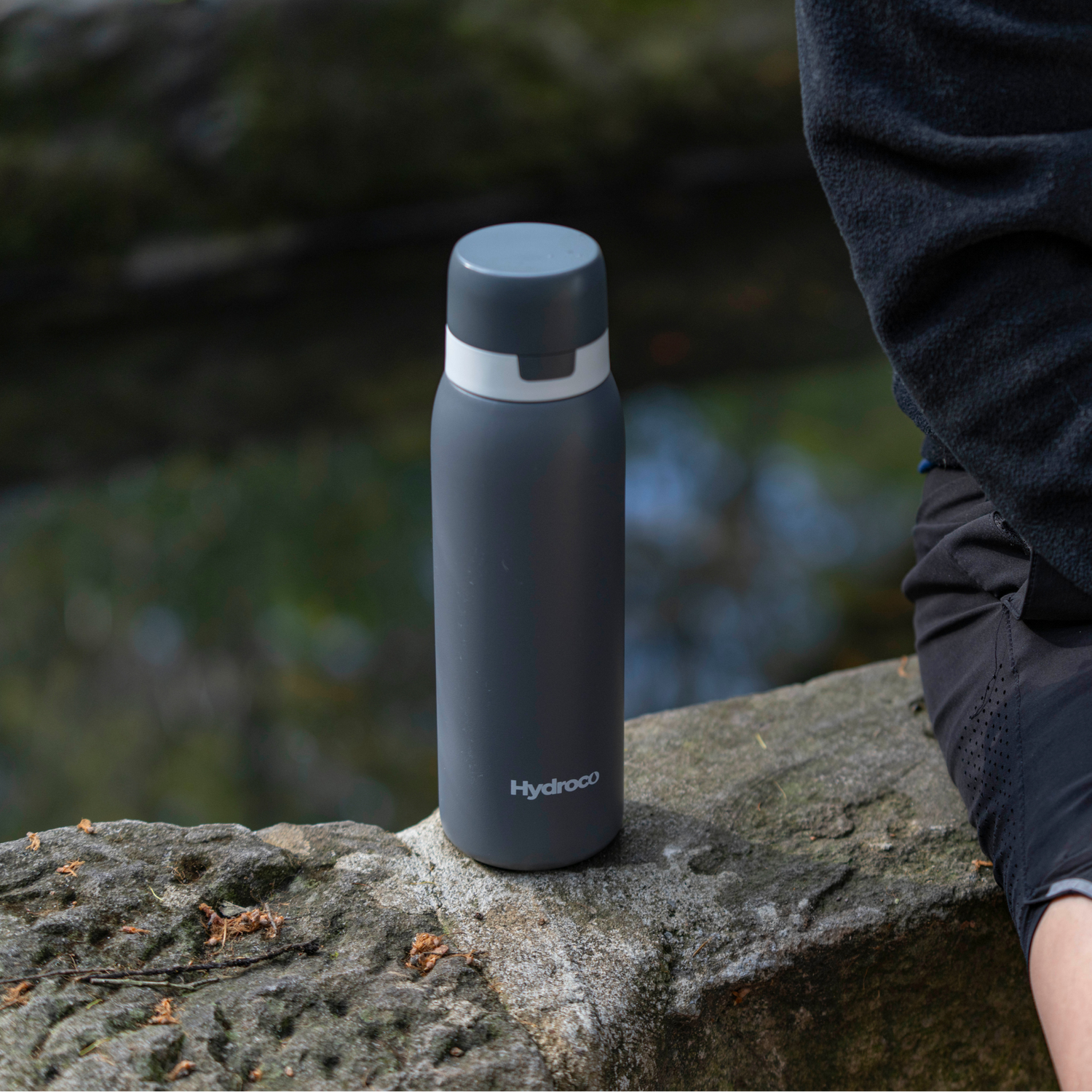 Black Hydroco flask bottle on a stone ledge with a blurred natural background